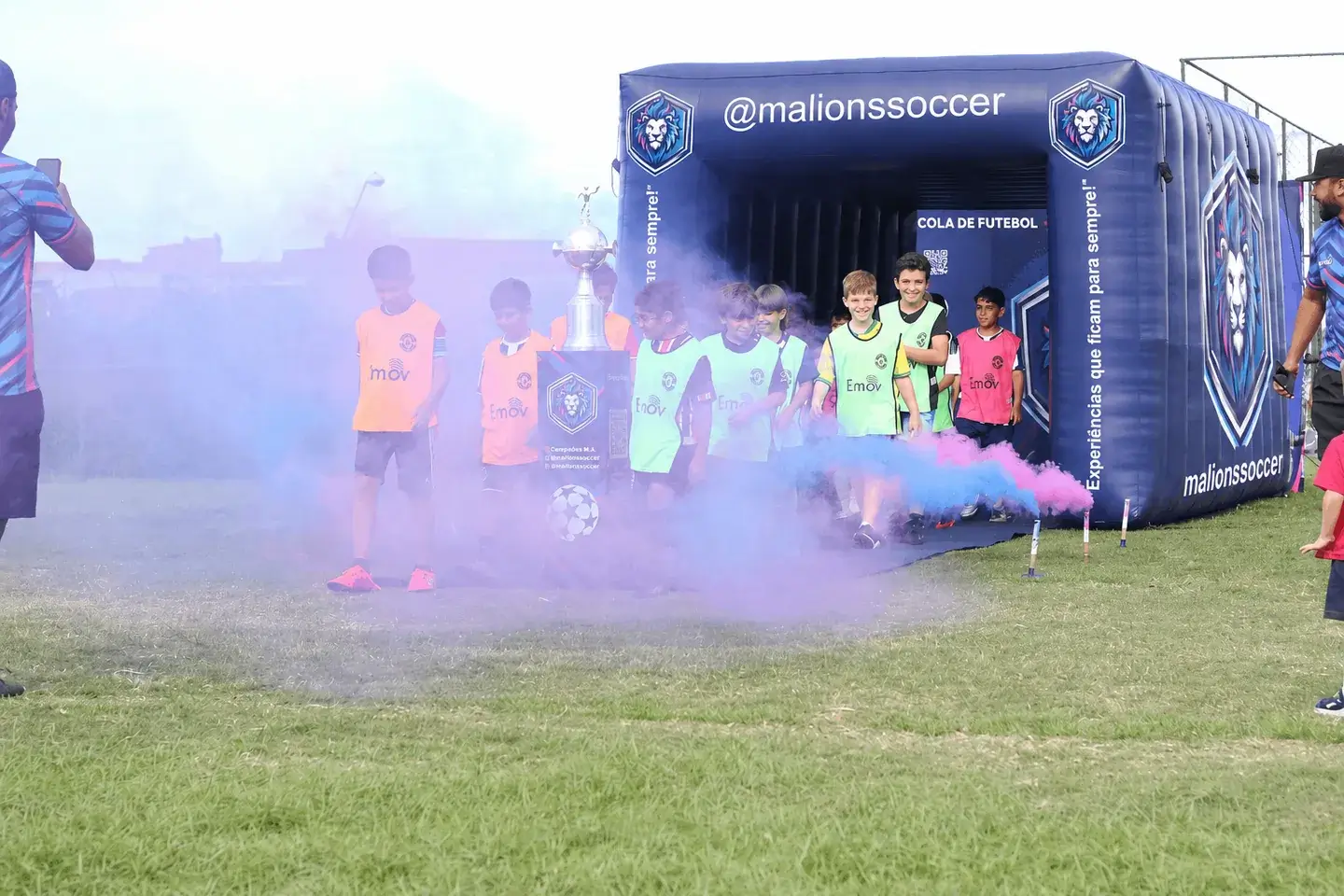 Crianças na entrada de um túnel de futebol com fumaça colorida