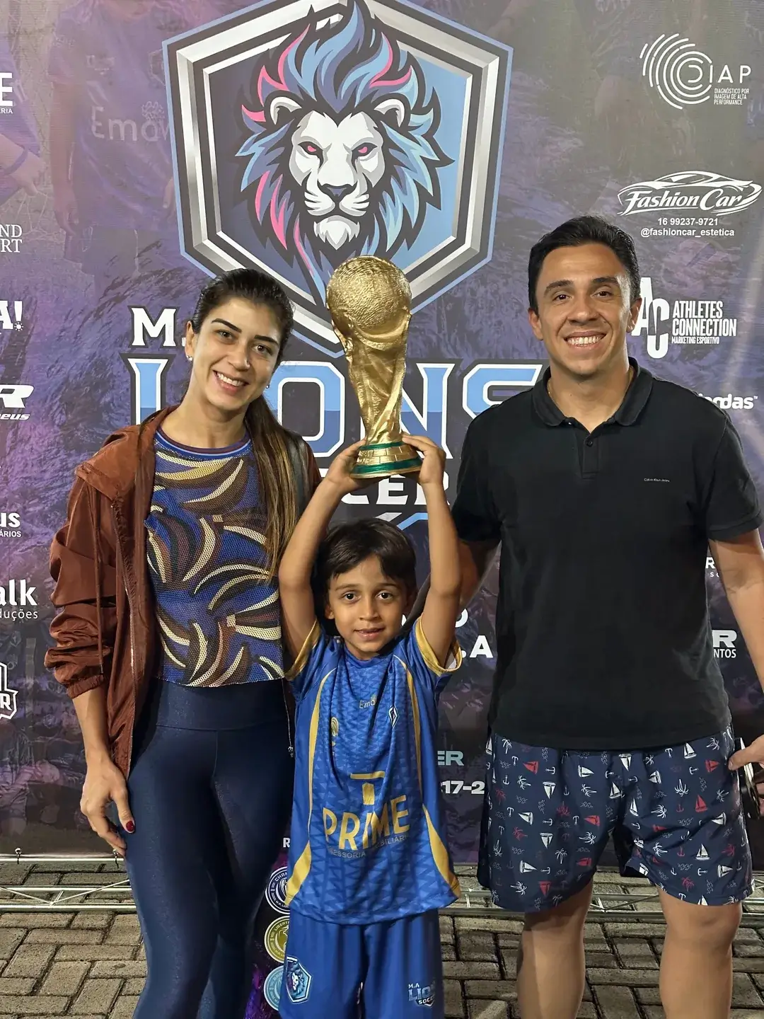 Criança com um troféu acompanhada por dois adultos no evento da Lions