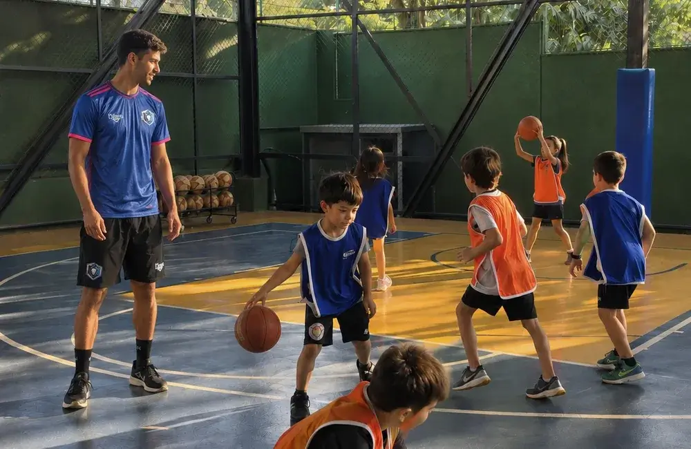 Professor orientando crianças com bolas em uma quadra coberta